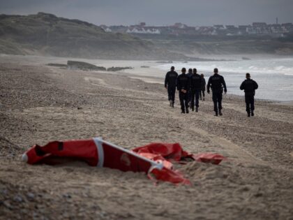 TOPSHOT - French police officers patrolling the beach between Ambleteusse and Wimereux, northern France, pass by the wreckage of a inflatable boat used by migrants who attempt to cross the Channel towards England, on October 16, 2021. (Photo by Marc SANYE / AFP) / The erroneous mention appearing in the …