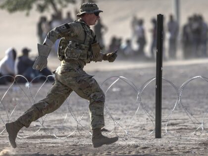EL PASO, TEXAS - MAY 10: A Texas National Guard soldier runs while setting up razor wire around a makeshift immigrant camp located between the Rio Grande and the U.S.-Mexico border fence on May 10, 2023 in El Paso, Texas. The number of immigrants reaching the border has surged with …