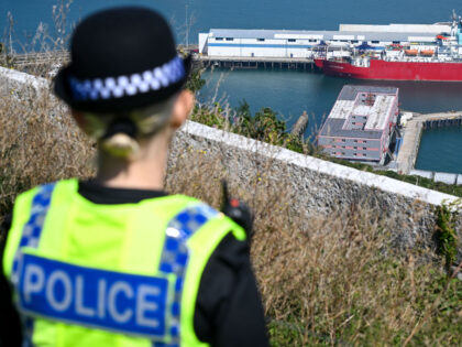 PORTLAND, ENGLAND - AUGUST 10: A Police officer looks out over the Bibby Stockholm immigration barge, at Portland Port, on August 10, 2023 in Portland, England. The first residents arrived on August 7th as the British government seeks to relocate asylum seekers from government-leased hotels. The Home Office says the …