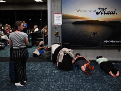 TOPSHOT - Passengers try to sleep below a "Welcome To Maui" billboard on the floor of the airport terminal while waiting for delayed and canceled flights off the island as thousands of passengers were stranded at the Kahului Airport (OGG) in the aftermath of wildfires in western Maui in Kahului, …